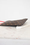 A Louis Vuitton monogram canvas small pouch in dark brown with gold LV logos, resting on a white marble surface against a white background.