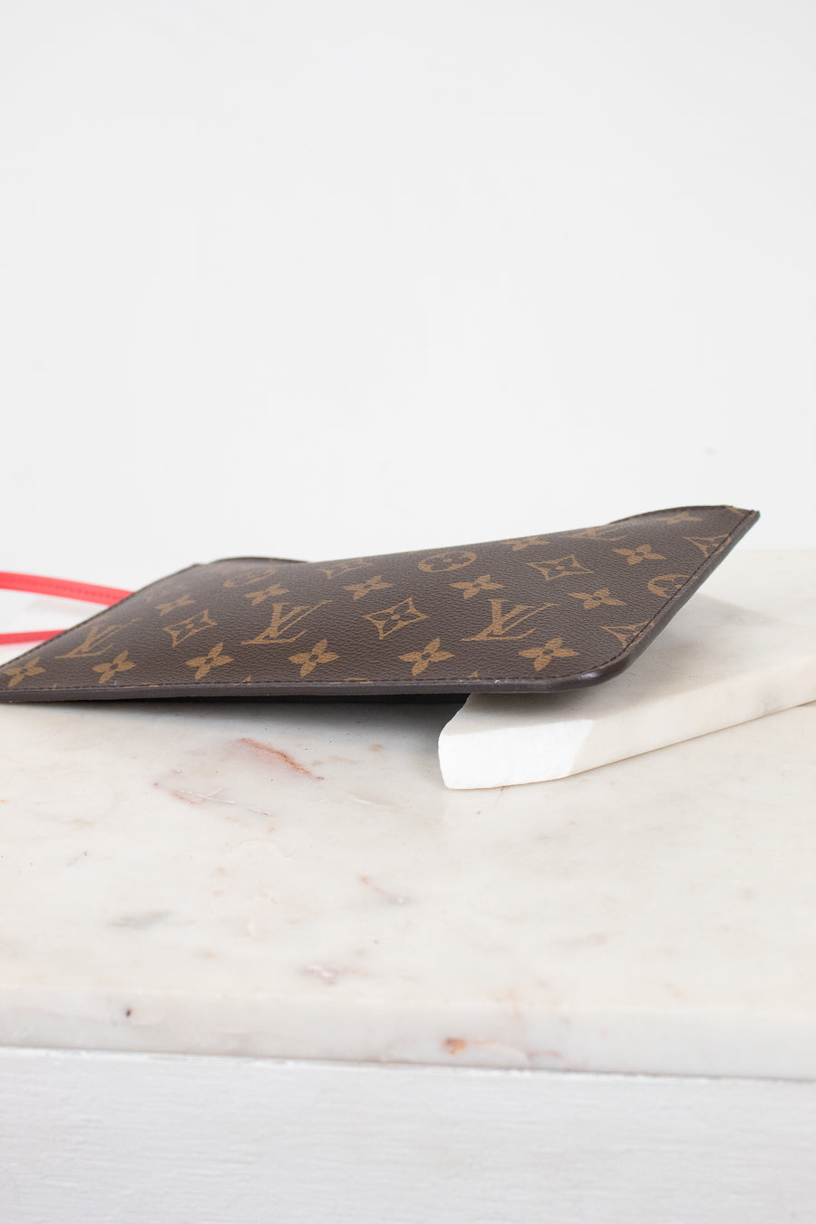 A Louis Vuitton monogram canvas small pouch in dark brown with gold LV logos, resting on a white marble surface against a white background.
