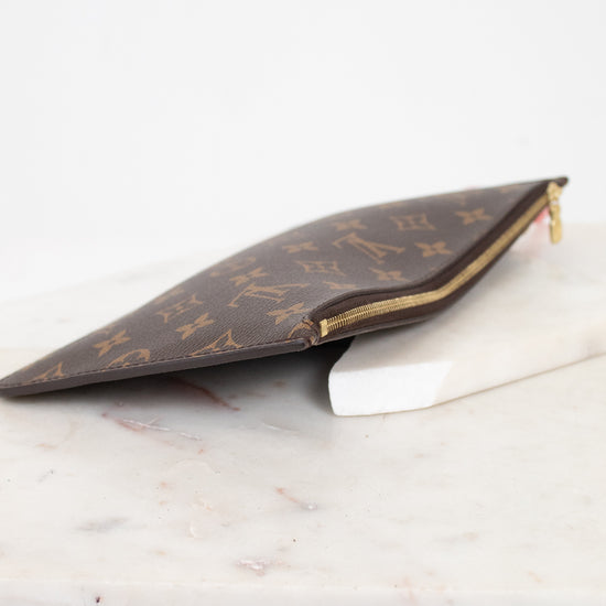 A Louis Vuitton monogram canvas zip pouch in brown and gold, resting on a white marble block against a white background.