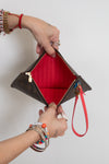 A Louis Vuitton monogram clutch pouch with a bright red interior lining and a red wristlet strap, held open by two hands wearing various bracelets and rings against a plain white background.