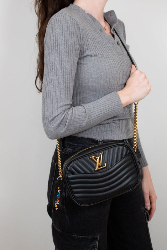 Woman wearing a black quilted handbag with gold chain strap against a plain background