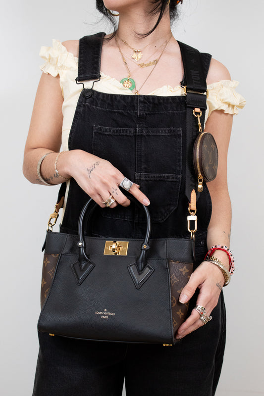 Person holding a black handbag with gold accents against a plain background