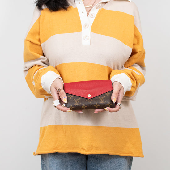 Person wearing a yellow and beige striped shirt holding a red wallet with a visible brand logo.