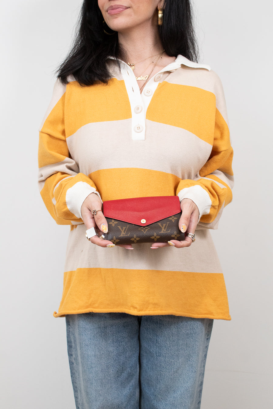 Person wearing a yellow and beige striped shirt holding a red wallet with a visible brand logo.