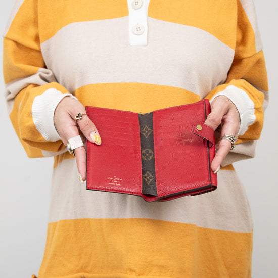 Person wearing a yellow and beige striped shirt holding a red wallet.