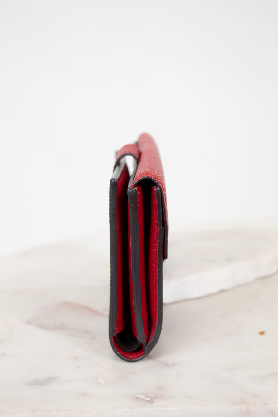Red leather side view of wallet on a white marble surface