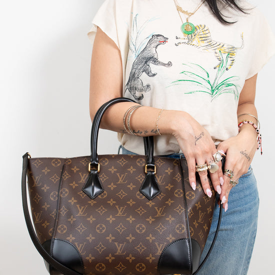 Person holding a brown patterned handbag with a plain background
