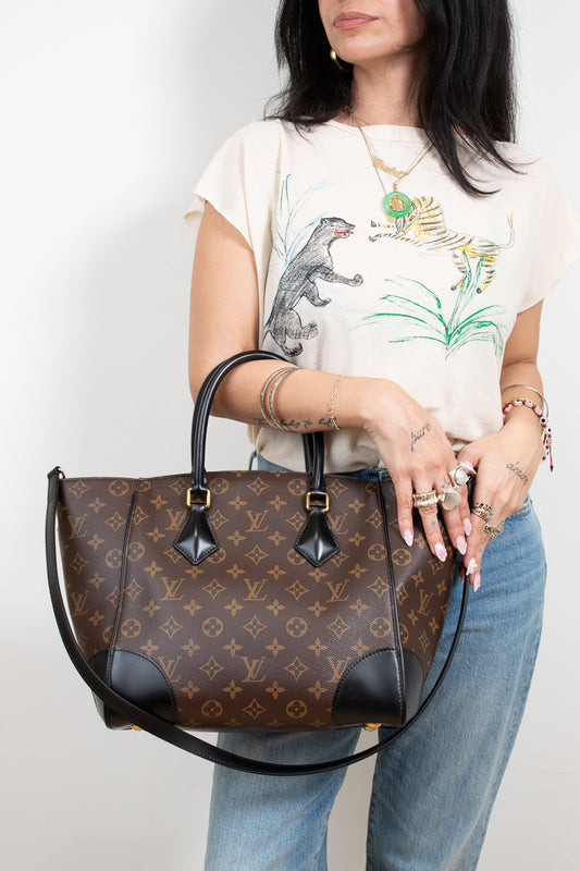 Person holding a brown patterned handbag with a plain background