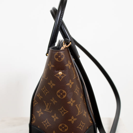Brown handbag with black accents and monogram pattern on a white background