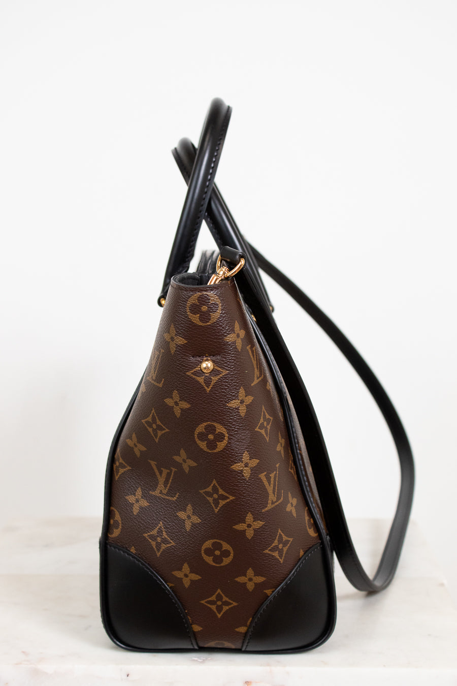 Brown handbag with black accents and monogram pattern on a white background