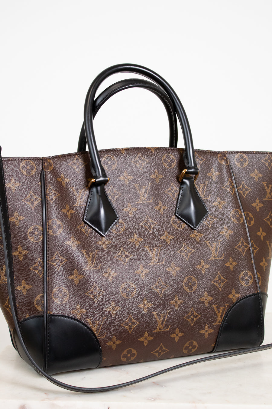 Designer handbag with monogram pattern and black accents on a light background