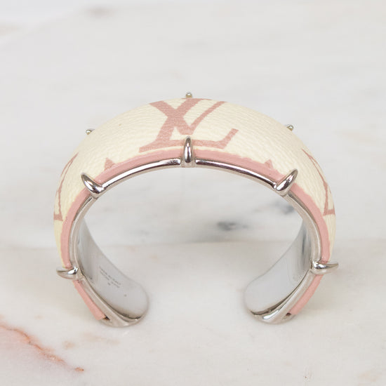 A Louis Vuitton cuff bracelet featuring the brand's signature beige and pink monogram canvas with a polished silver-tone metal spiky frame, resting on a white marble surface.