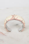 A Louis Vuitton cuff bracelet featuring the brand's signature beige and pink monogram canvas with a polished silver-tone metal spiky frame, resting on a white marble surface.