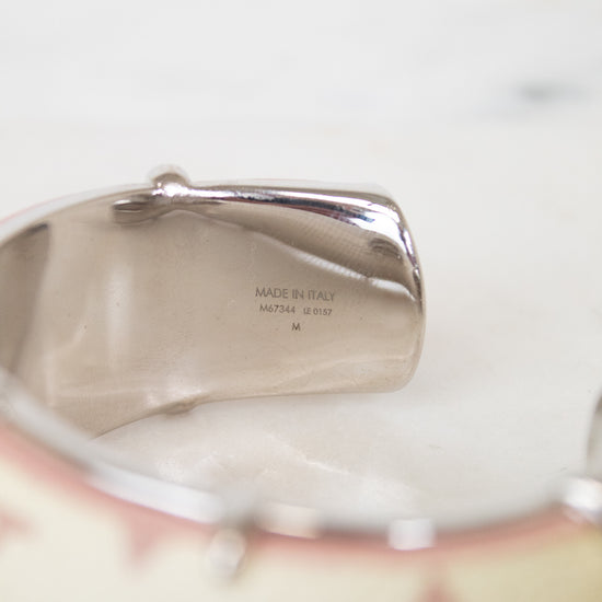 Close-up of a silver-toned cuff bracelet showing engraved details and a portion of a cream-colored patterned band with pink floral motifs.