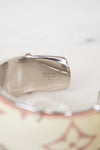 Close-up of a silver-toned cuff bracelet showing engraved details and a portion of a cream-colored patterned band with pink floral motifs.