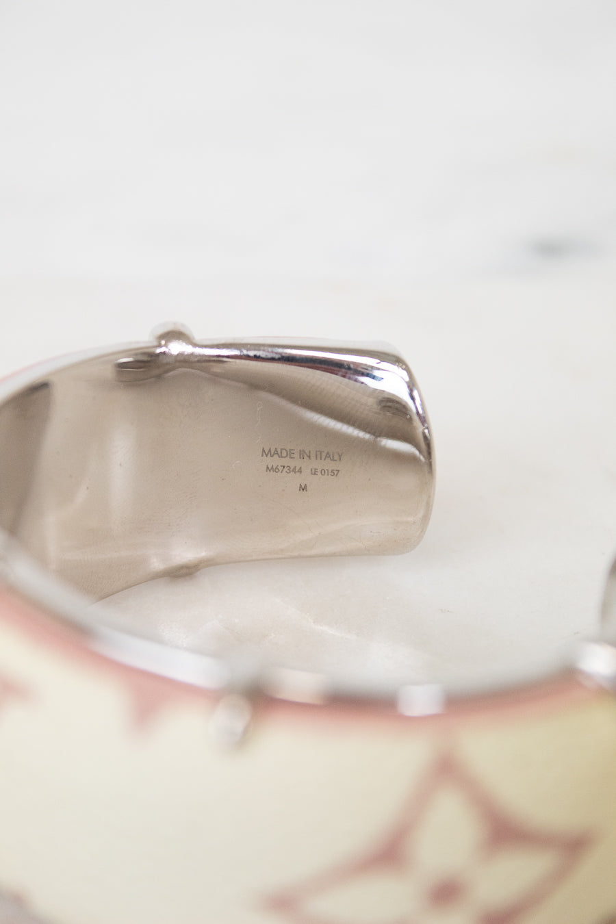 Close-up of a silver-toned cuff bracelet showing engraved details and a portion of a cream-colored patterned band with pink floral motifs.