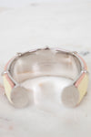 A Louis Vuitton cuff bracelet with a silver-tone metal band, featuring pale yellow and light pink enamel inlays, resting on a white marble surface.