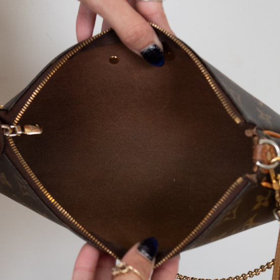 Brown handbag with gold accents held open by a hand on a neutral background