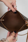 Brown handbag with gold accents held open by a hand on a neutral background