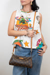Person wearing a colorful sleeveless top with graphic designs and holding a brown handbag.
