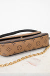 A Louis Vuitton monogram canvas shoulder bag in tan and brown, featuring a black leather strap and a gold-tone chain link detail, displayed on a white marble surface against a white background.