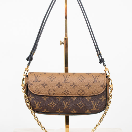 Louis Vuitton monogram shoulder bag in brown and beige coated canvas with gold-tone hardware, displayed on a gold stand against a white background.