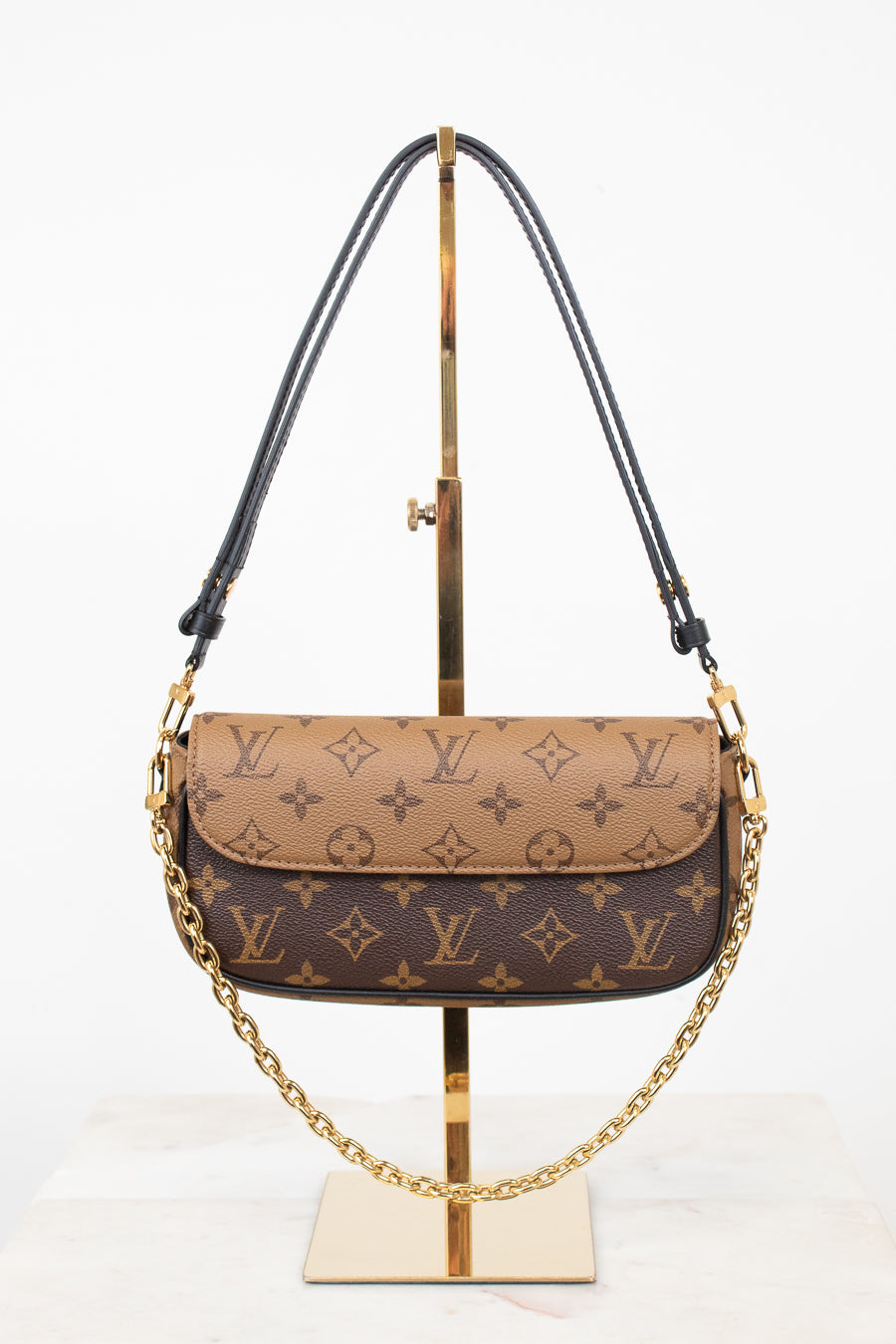 Louis Vuitton monogram shoulder bag in brown and beige coated canvas with gold-tone hardware, displayed on a gold stand against a white background.