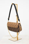 Louis Vuitton monogram shoulder bag in brown coated canvas with a black leather shoulder strap and gold-tone chain detail, displayed on a gold stand against a white background.