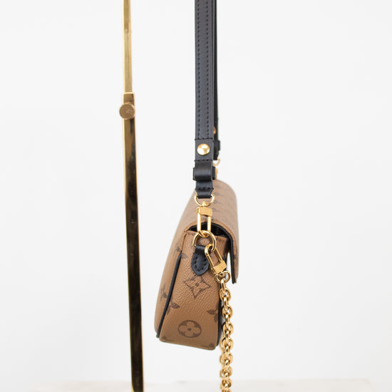 A Louis Vuitton monogram shoulder bag in brown coated canvas with a black leather strap and gold-tone chain, displayed on a gold metal stand against a white background.