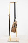 A Louis Vuitton monogram shoulder bag in brown coated canvas with a black leather strap and gold-tone chain, displayed on a gold metal stand against a white background.