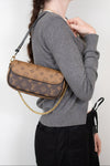 A woman wearing a gray long-sleeve top and black pants carries a Louis Vuitton monogram shoulder bag with a gold chain strap against a plain white background.