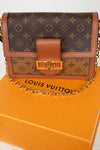 Louis Vuitton monogram shoulder bag in brown coated canvas with tan leather trim and a gold-tone chain strap, displayed on top of an orange Louis Vuitton box.