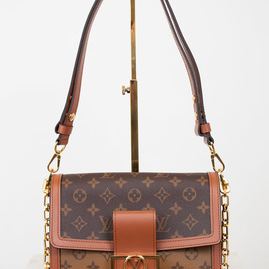 A Louis Vuitton monogram shoulder bag in brown coated canvas with tan leather trim and gold-tone hardware, displayed on a stand against a white background.