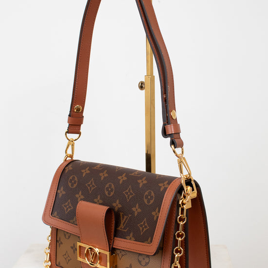 A Louis Vuitton shoulder bag in brown monogram coated canvas with tan leather trim and gold-tone hardware, displayed on a stand against a clean white background.