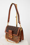 A Louis Vuitton shoulder bag in brown monogram coated canvas with tan leather trim and gold-tone hardware, displayed on a stand against a clean white background.