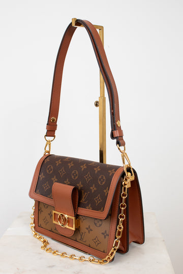 A Louis Vuitton shoulder bag in brown monogram coated canvas with tan leather trim and gold-tone hardware, displayed on a stand against a clean white background.