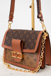 A Louis Vuitton shoulder bag in brown monogram coated canvas with tan leather trim and a gold-tone chain strap, displayed on a stand against a light background.