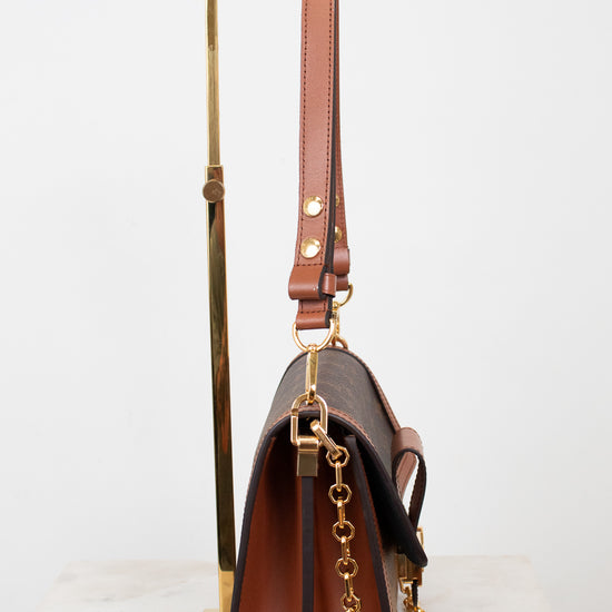 A brown leather shoulder bag with gold-tone hardware, displayed on a gold metal stand against a white background.