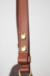 Close-up of a brown leather strap with gold-tone metal rivets and hardware, shown against a plain light gray background.