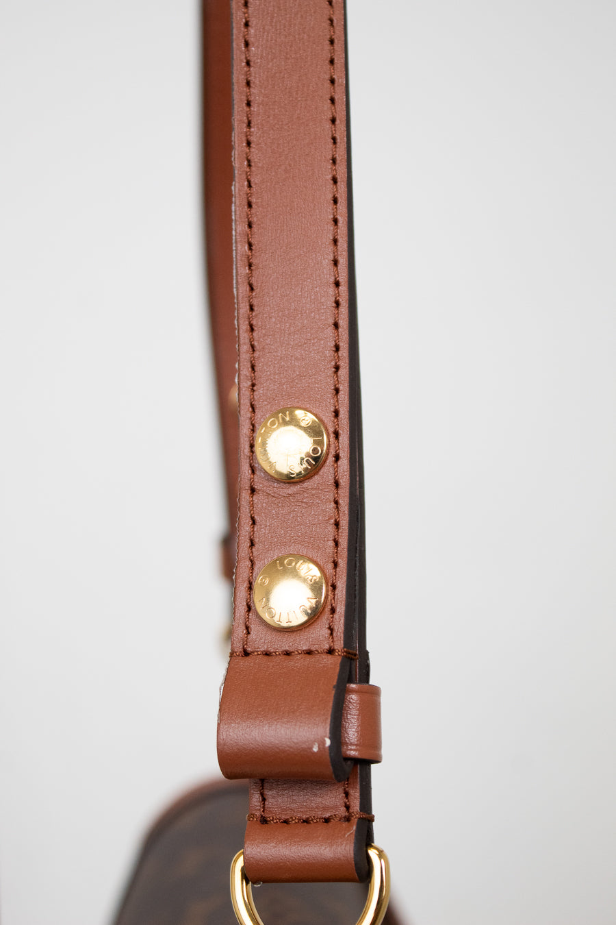 Close-up of a brown leather strap with gold-tone metal rivets and hardware, shown against a plain light gray background.