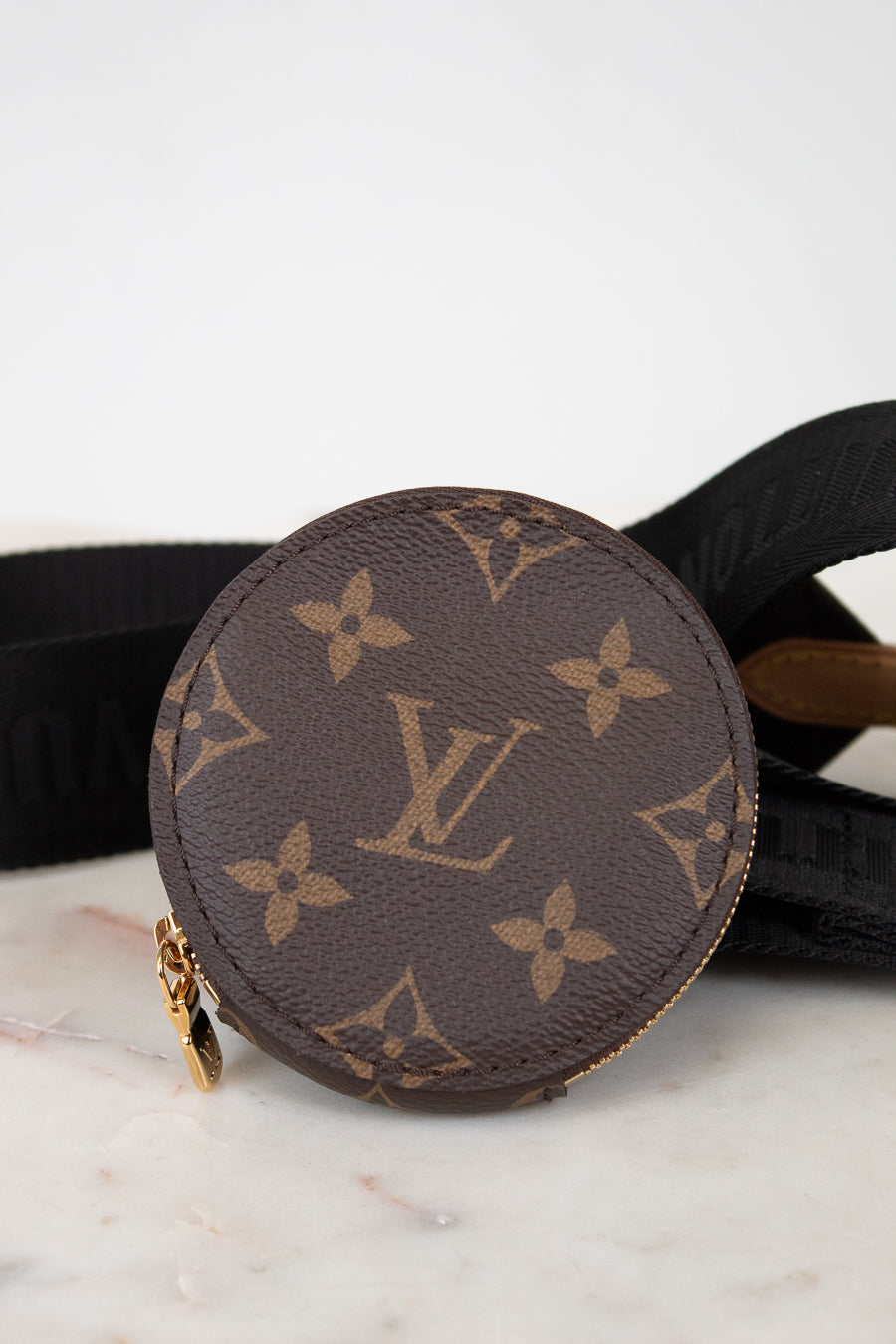 Round brown Louis Vuitton coin purse with monogram pattern on a marble surface.