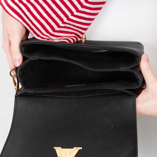 Black handbag with gold logo held by a person wearing red and white striped sleeves.