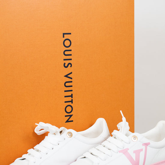White and pink sneakers with Louis Vuitton logo in front of an orange Louis Vuitton box.