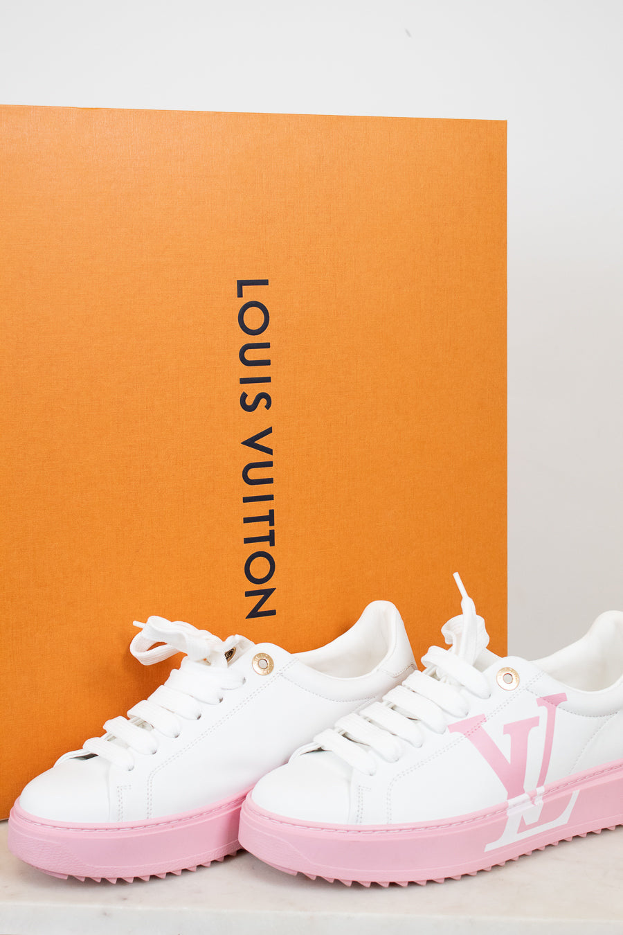White and pink sneakers with Louis Vuitton logo in front of an orange Louis Vuitton box.