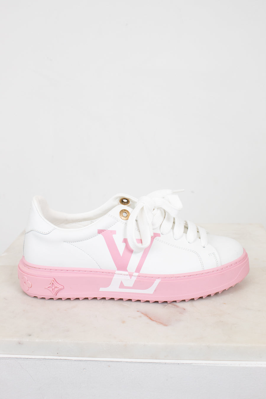 White sneaker with pink sole and logo on a light gray background