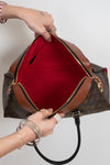 Brown handbag with red interior being held open by a person on a light gray background