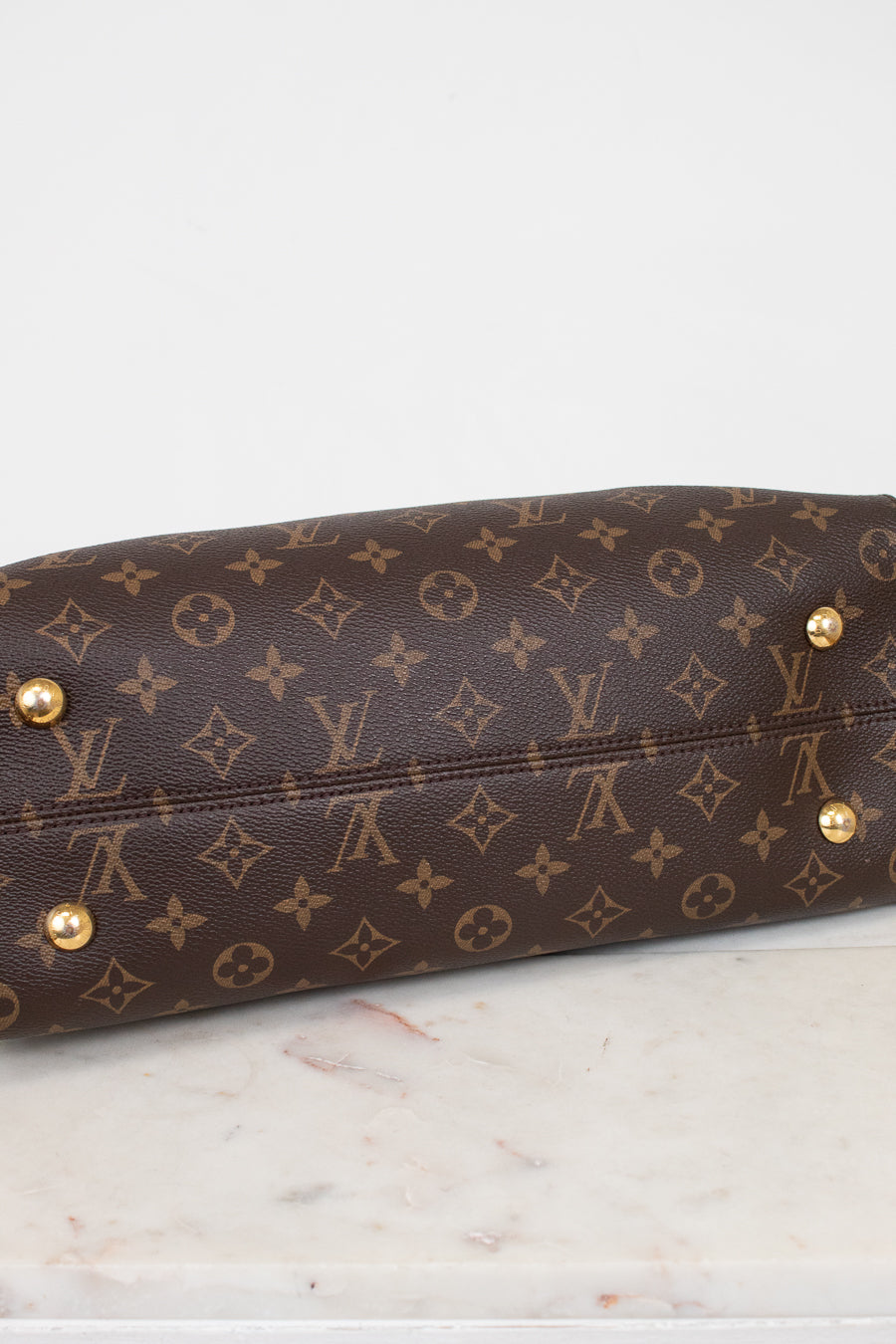 Brown leather handbag with gold studs on a marble surface