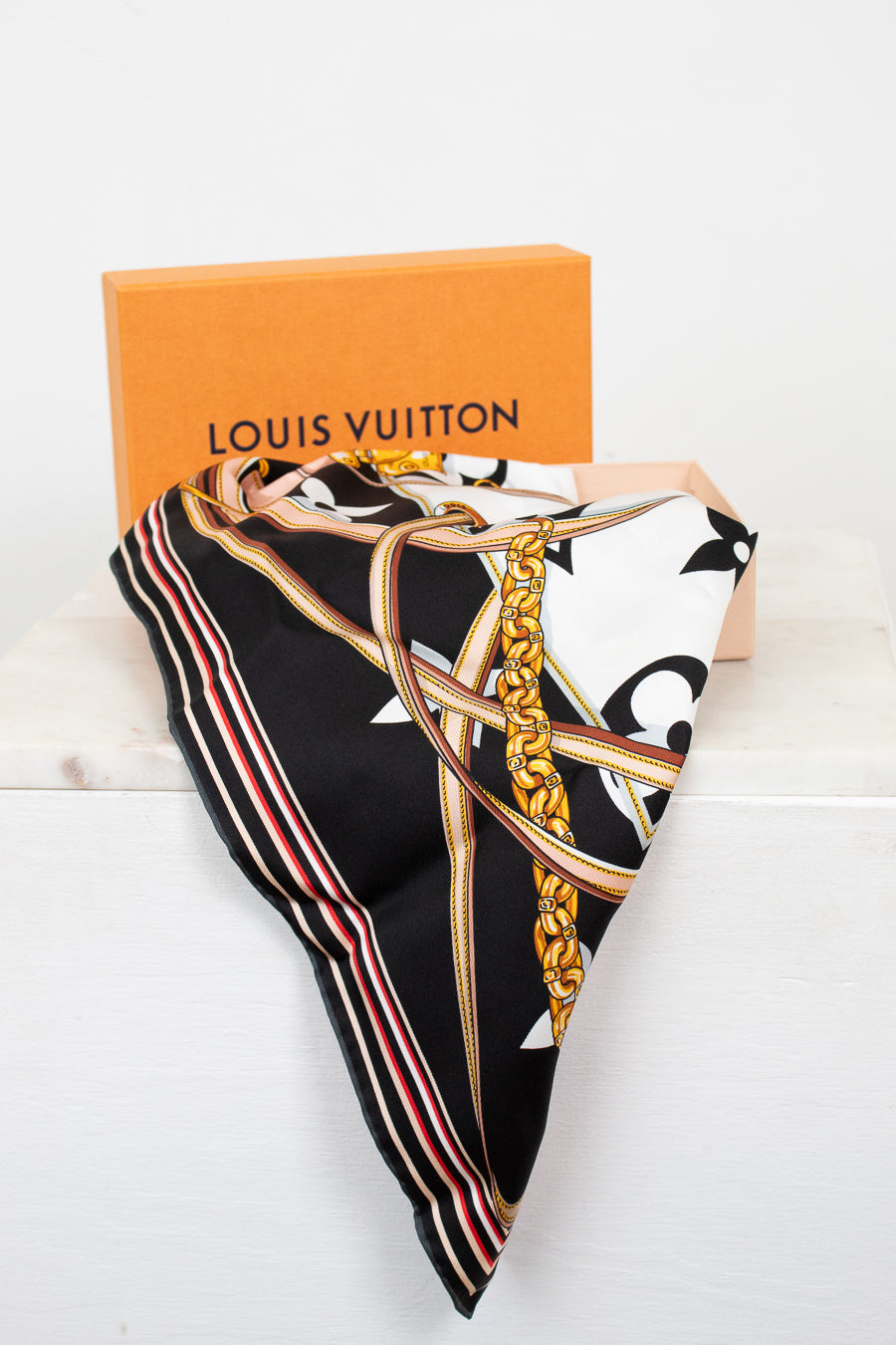 Louis Vuitton scarf with decorative chain print folded with orange box on a white background