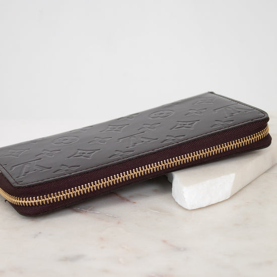 Maroon patent leather wallet with gold zipper on a marble surface