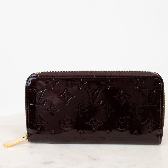 Maroon patent leather wallet with brand logo on a white marble surface